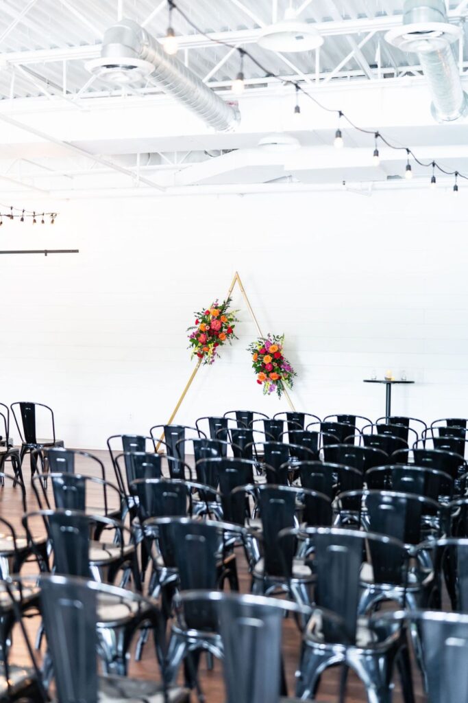 Black metal chairs set up for a wedding ceremony with a gold arch and bright florals