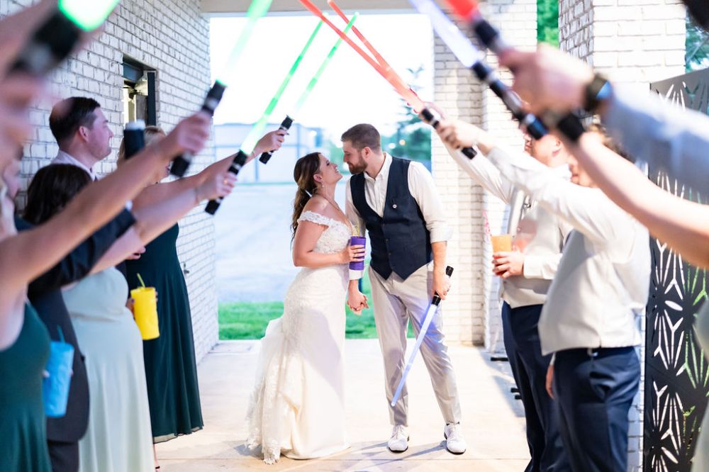 A bride and groom doing a send-off on their wedding day at BASH with light sabers