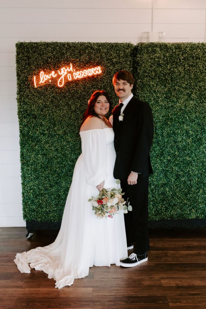 Bride and groom in front of green hedge wall