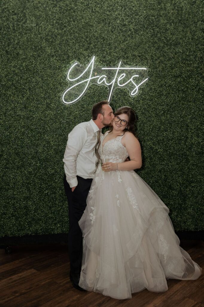 Bride and groom in front of BASH's greenery wall